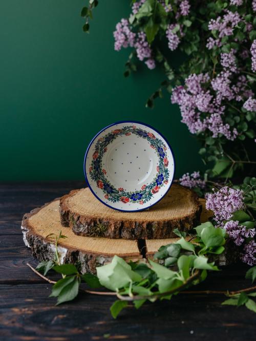 Mała ceramiczna miska umieszczona bokiem na drewnianych deskach wśród fioletowych bzów.