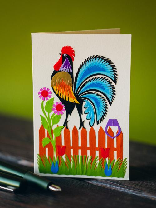 kartka wycinanka kogut z niebieskim ogonem na płocie