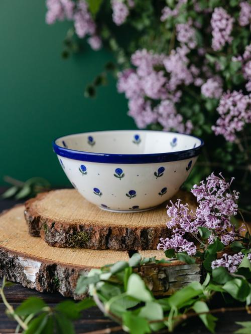 Ceramiczna miska umieszczona bokiem na drewnianych deskach wśród fioletowych bzów.