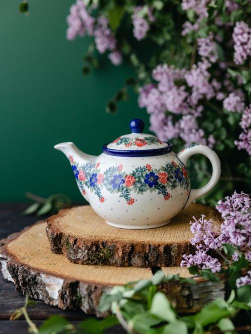 Ceramiczny czajnik umieszczony bokiem na drewnianych deskach wśród fioletowych bzów.