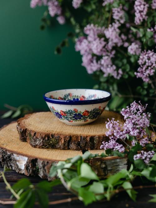 Mała ceramiczna miska umieszczona bokiem na drewnianych deskach wśród fioletowych bzów.