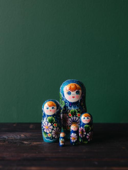 Pięć matrioszek stojących zbiorczo, blisko siebie na drewnianym stole na tle zielonej ściany.
