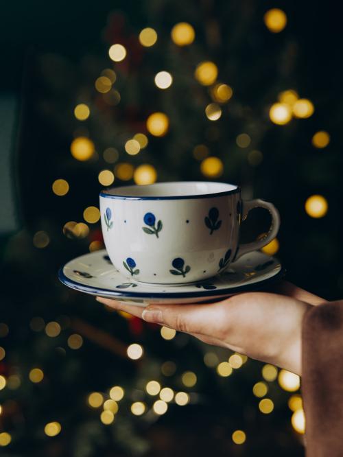 filiżanka z podstawkiem trzymana w dłoni