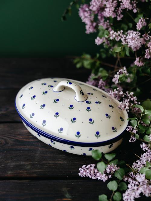 Ceramiczna zapiekanka z pokrywką uchwycona pod skosem na tle bzów.