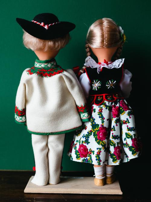 Lalki tyłem w strojach góralskich na zielonym tle.