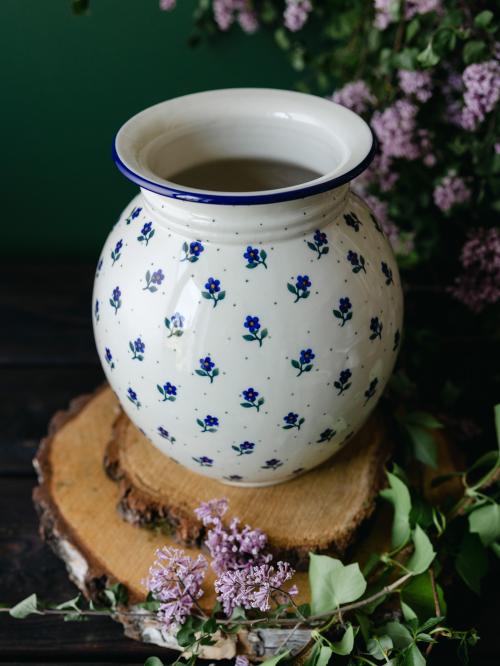 Wielki, ceramiczny wazon uchwycony delikatnie z góry stojąc na drewnianych deseczkach na tle fioletowych bzów.