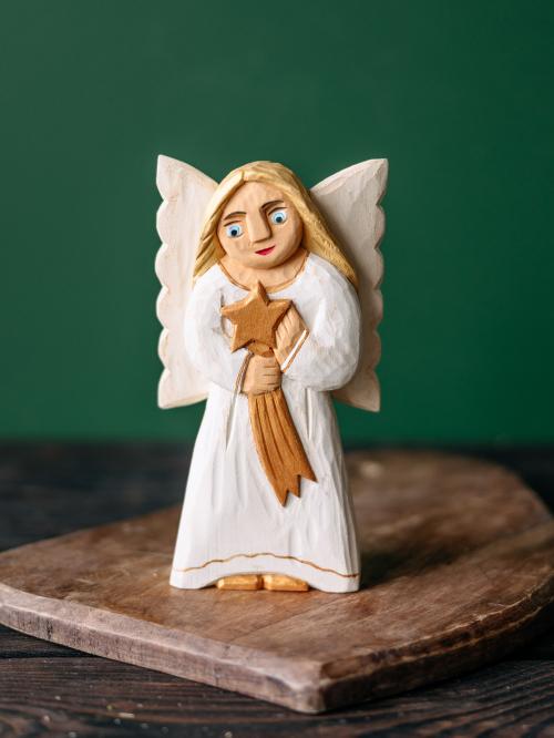 anioł rzeźbiony w białej sukience na tle zielonej ściany