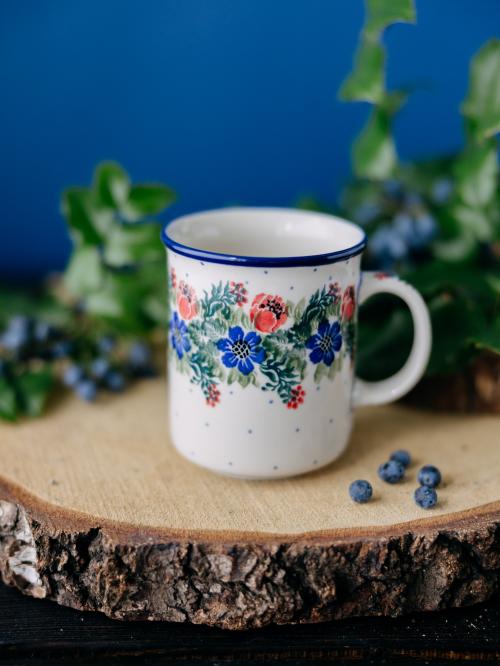 Kubek ceramiczny na drewnianym stole na tle roślin.