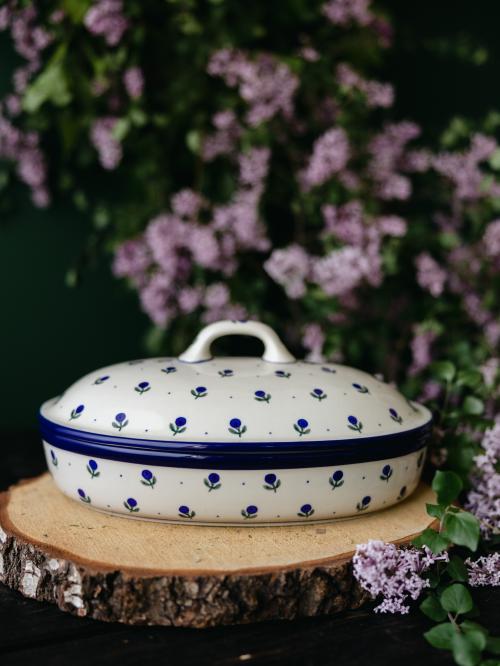 Ceramiczna zapiekanka z pokrywką uchwycona przodem na tle bzów.