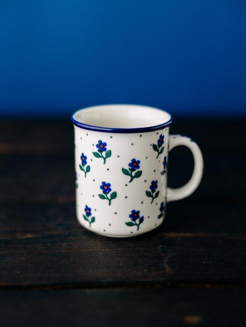 Kubek ceramiczny  na drewnianym stole na tle roślin.