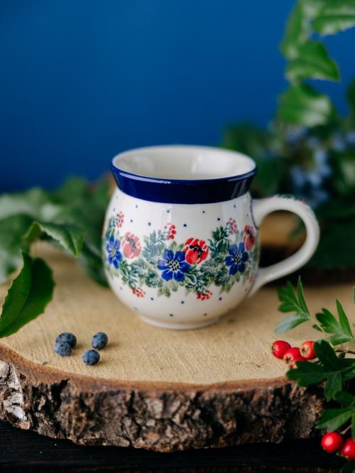 Kubek ceramiczny na drewnianym stole na tle roślin.