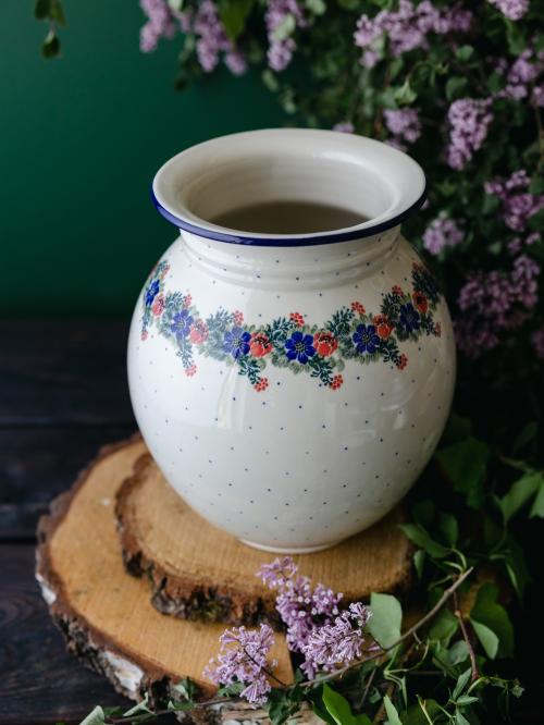 Wielki, ceramiczny wazon uchwycony delikatnie z góry stojąc na drewnianych deseczkach na tle fioletowych bzów.