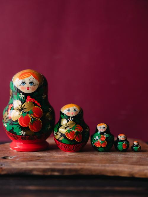 Pięć matrioszek stojących w rzędzie na drewnianym stole na tle zielonej ściany.