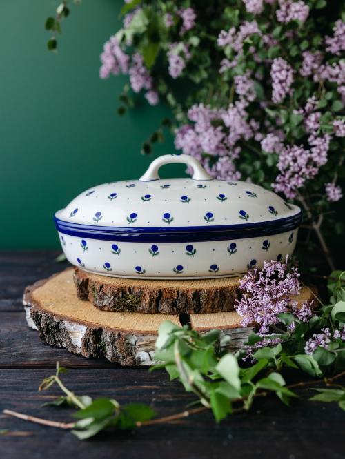 Ceramiczna zapiekanka z pokrywką uchwycona przodem na tle bzów.