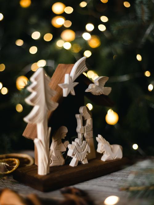 Drewniana szopka bokiem na tle choinki.