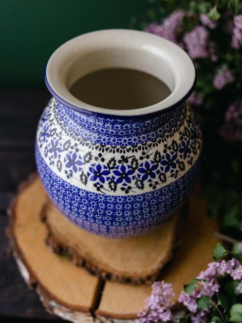 Wielki, ceramiczny wazon uchwycony delikatnie z góry stojąc na drewnianych deseczkach na tle fioletowych bzów.