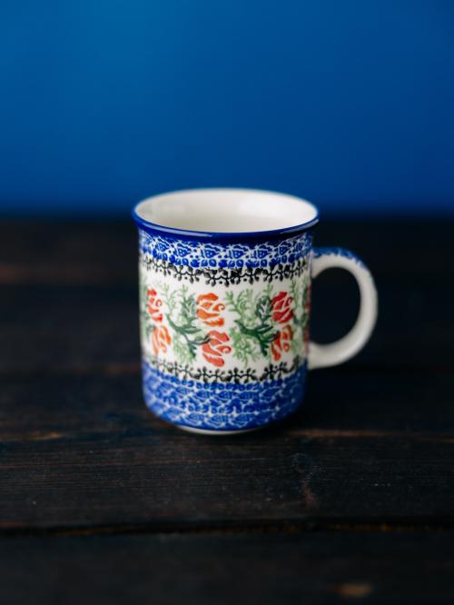 Kubek ceramiczny na drewnianym stole na tle roślin.