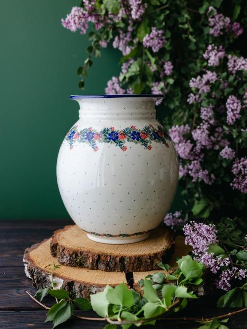 Wielki, ceramiczny wazon uchwycony przodem stojąc na drewnianych deseczkach na tle fioletowych bzów.