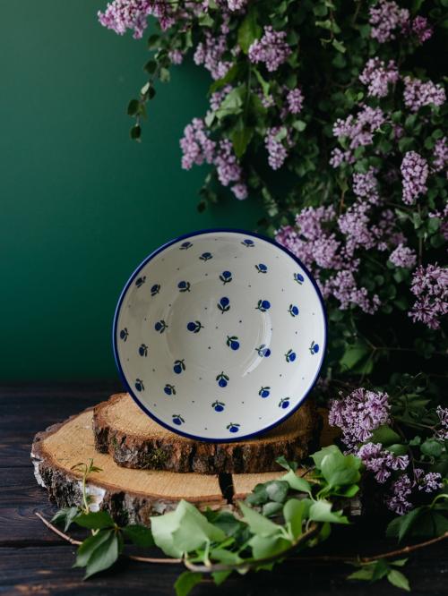 Ceramiczna miska umieszczona na boku na drewnianych deskach wśród fioletowych bzów.