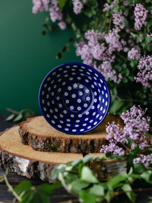 Zbliżenie na wnętrze ceramicznej miski umieszczonej na drewnianej desce wśród fioletowych bzów.