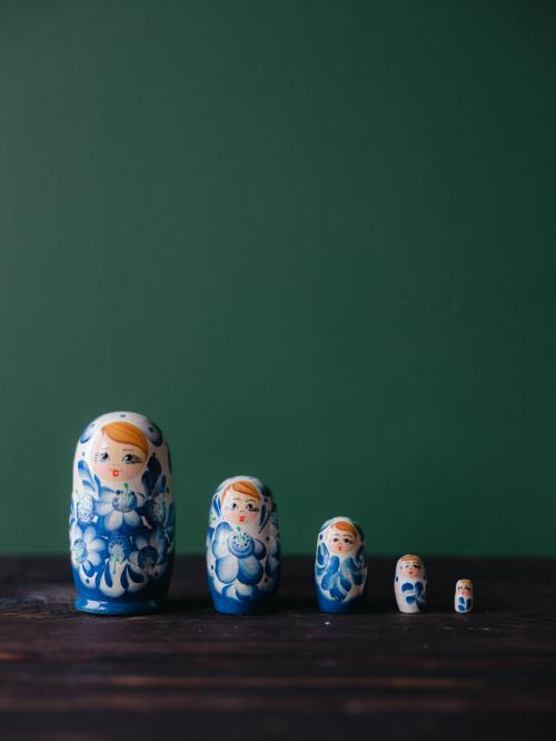Pięć matrioszek stojących w rzędzie na drewnianym stole na tle zielonej ściany.