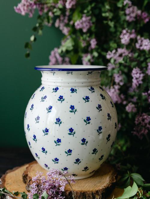 Wielki, ceramiczny wazon uchwycony przodem stojąc na drewnianych deseczkach na tle fioletowych bzów.