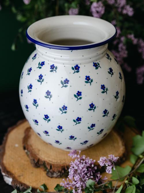 Wielki, ceramiczny wazon uchwycony delikatnie z góry stojąc na drewnianych deseczkach na tle fioletowych bzów.