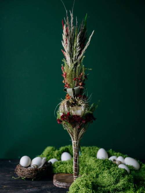 Zbliżenie na wielkanocną palemkę z suszonych składników na tle zielonej ściany.