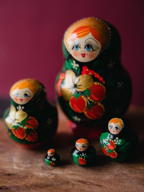 Pięć matrioszek stojących zbiorczo, blisko siebie na drewnianym stole na tle zielonej ściany.