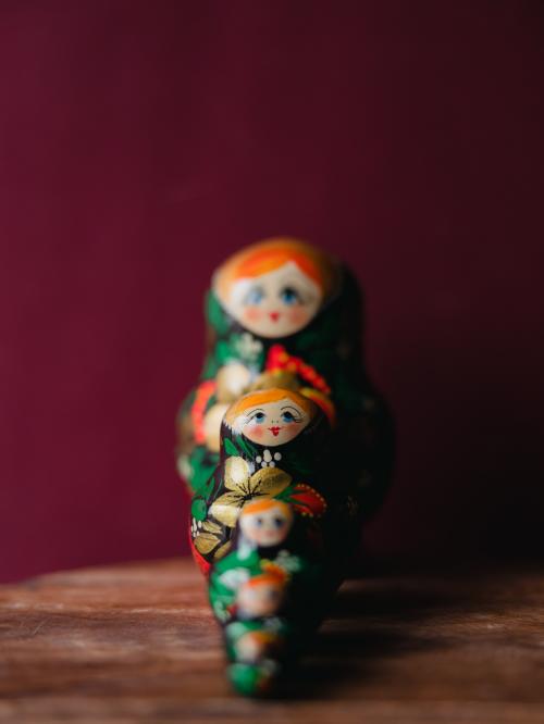 Pięć matrioszek stojących w rzędzie na drewnianym stole na tle zielonej ściany.