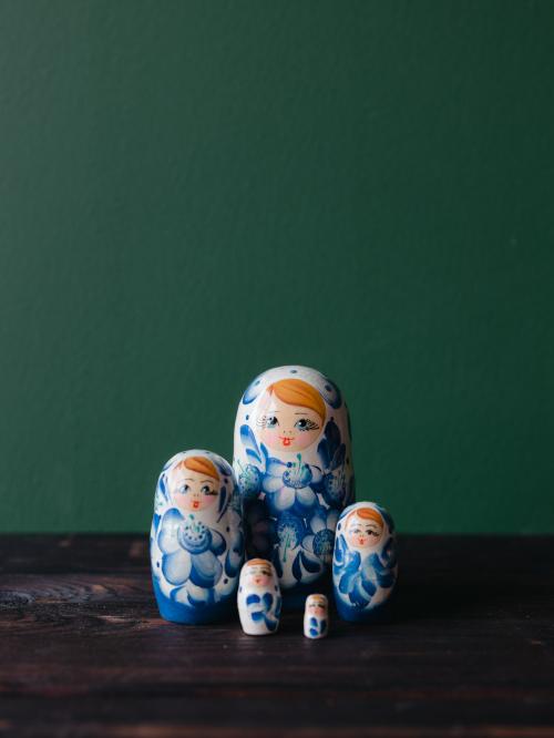 Pięć matrioszek stojących zbiorczo, blisko siebie na drewnianym stole na tle zielonej ściany.